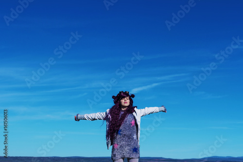 Mujer joven con los brazos extendidos y un gran cielo azul de fondo 