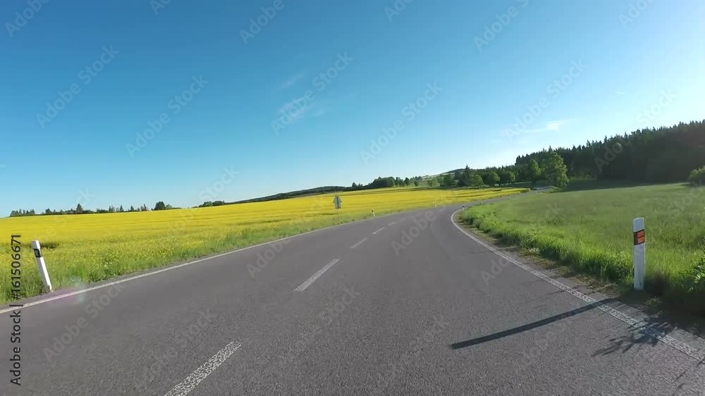Car drive in evening spring rural countryside road on a sunny day between field and meadow. Landscape with trees and blue sky with sunlight. Car drive in evening spring rural countryside road on a sunny day between field and meadow. Landscape with trees and blue sky with sunlight.