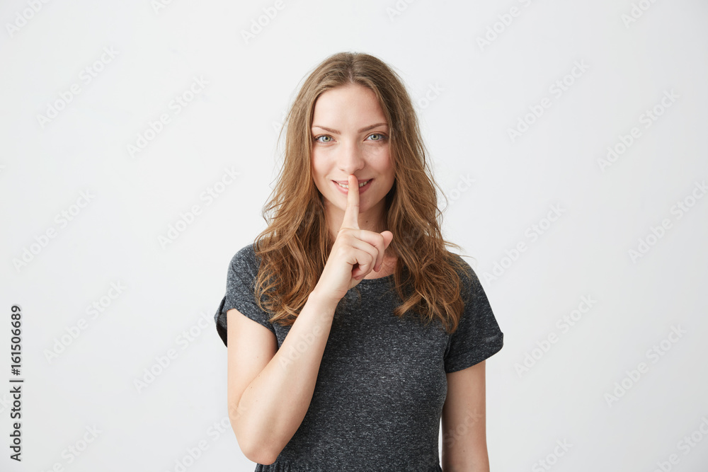 Portrait of young pretty tender girl smiling looking at camera straight showing keep silence over white background. Portrait of young pretty tender girl smiling looking at camera straight showing keep silence over white background.