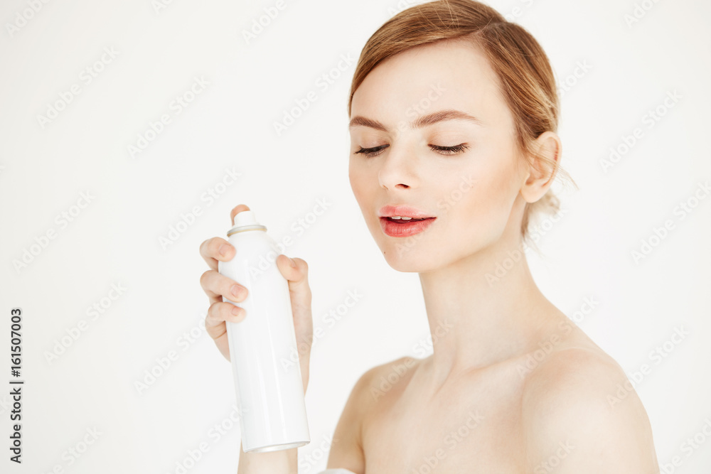 Nude beautiful blonde girl with fresh perfect skin smiling looking at camera holding cosmetology spray bottle over white background. Nude beautiful blonde girl with fresh perfect skin smiling looking at camera holding cosmetology spray bottle over white background.