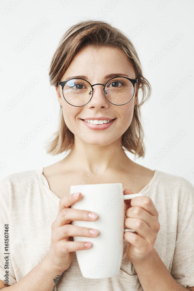 Cute beautiful girl in glasses smiling looking at camera holding cup over white background. Cute beautiful girl in glasses smiling looking at camera holding cup over white background.