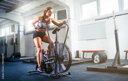 Woman at crossfit gym using exercise bike for cardio workout photo