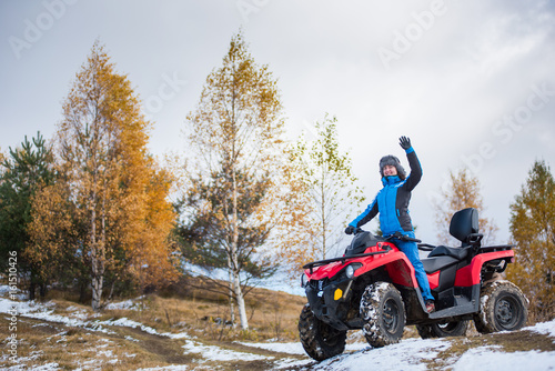 Φωτογραφία Happy female rider in blue winter clothes waving on a red quadbike atv on snow-c