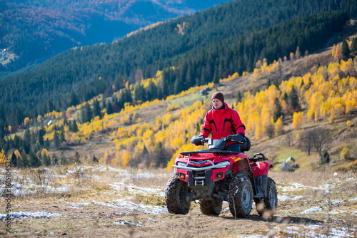 Man is riding up on a atv on a mountain road. Beautiful landscape of mountains woodlands with a variety of color of the trees green, yellow on the background