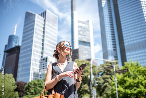 Lifestyle portrait of a businesswoman with phone and bag in the modern district in Frankfurt city