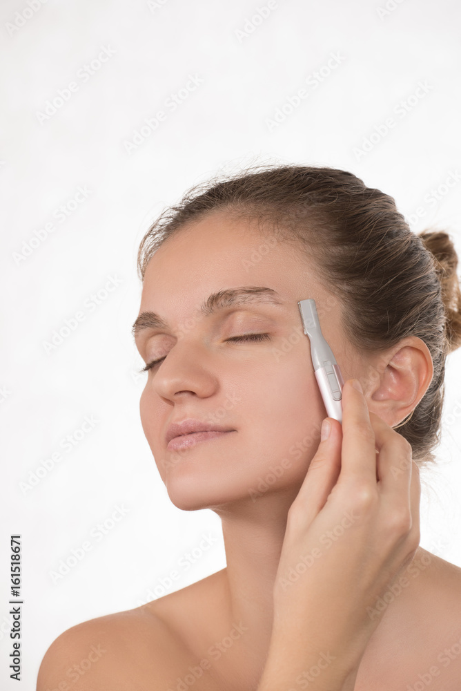 Young girl in a red towel caring for your eyebrows with trimmer
