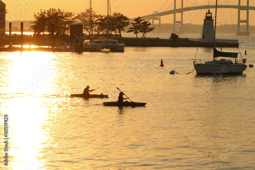 Two kayakers are out i the evening water, near the Newport Pell Bridge in Newport, Rhode Island