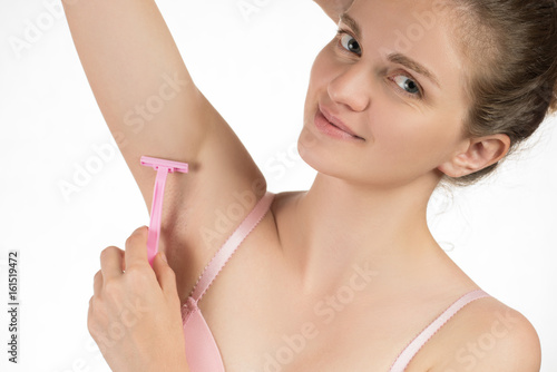 Beautiful young woman in a brazier smiling and doing depilation of armpits or shaving underarms with a pink razor on a white background