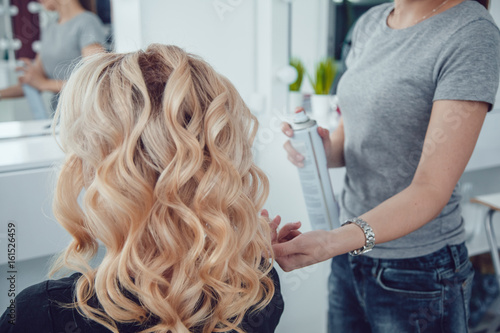 Hair stylist makes a curls for a girl, using hair styling. Hairdresser at work.