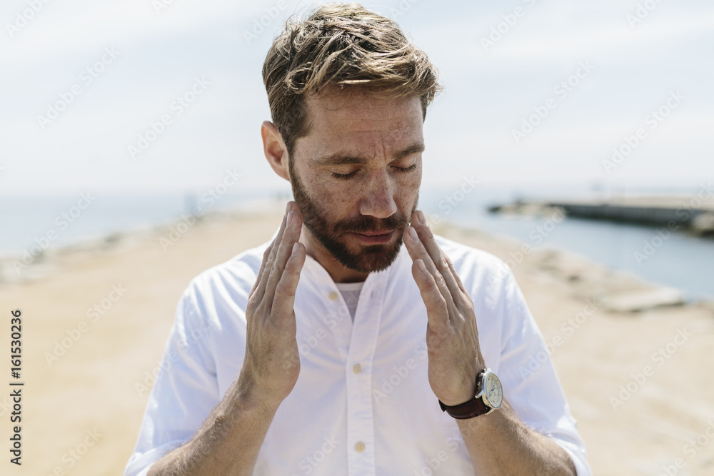 Mid adult man on the beach touching his face Mid adult man on the beach touching his face