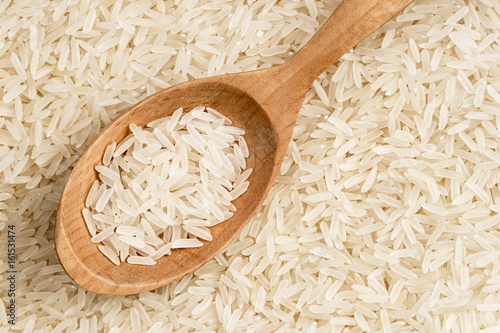 Close up of wooden spoon on background of long parboiled rice. Top view, high resolution product. Healthy food concept