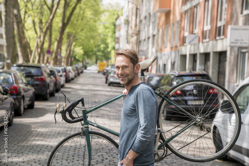 Portrait of smiling mature man carrying his bicycle on the shoulder