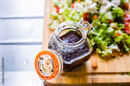 A Glass Bottle with Salad Dressing consisting of Balsamic Vinegar, Olive Oil, Pepper and Salt, Salad on the Background
