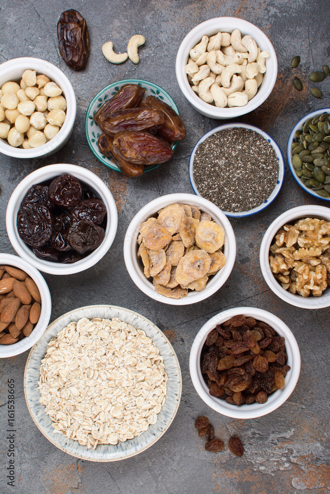Above view of ingredients for homemade granola, oats, different nuts and raisins, dates, seed on the grey stone background, selective focus Above view of ingredients for homemade granola, oats, different nuts and raisins, dates, seed on the grey stone background, selective focus