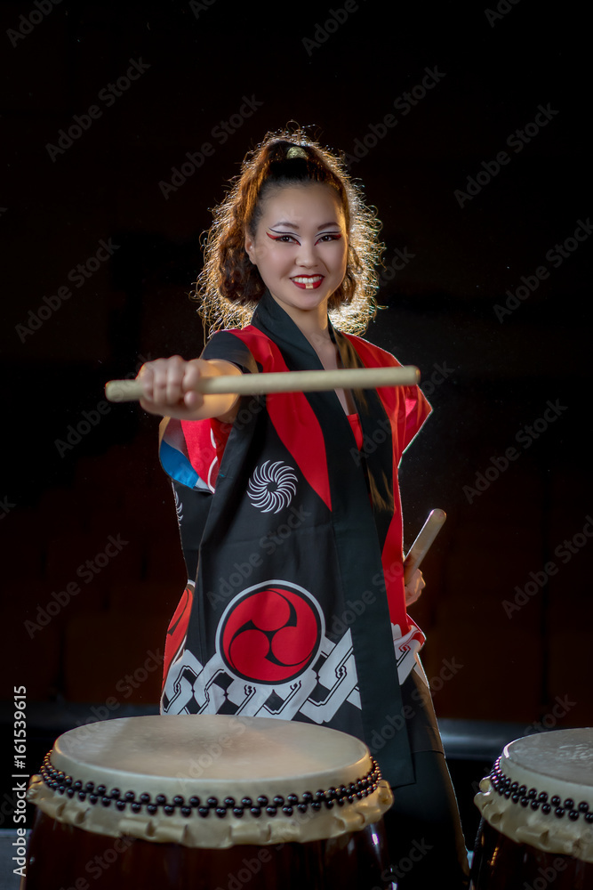 Fototapeta premium beautiful asian taiko drummer girl in red with drumsticks, studio shot on a dark background.