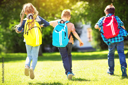 Obraz na plátne Children with rucksacks standing in the park near school