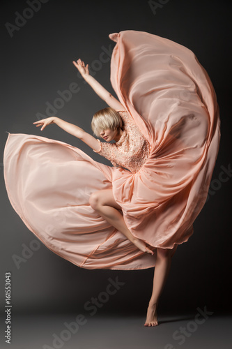 Woman in light chiffon dress dancing sensually on black plain background.