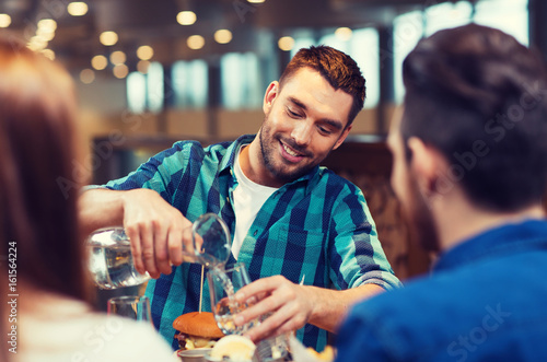 happy man with friends pouring water at restaurant