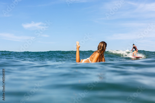 Sticker Two beautiful fit surfing girl in sexy bikini on surf surfboard board on sunrise or sunset in the ocean