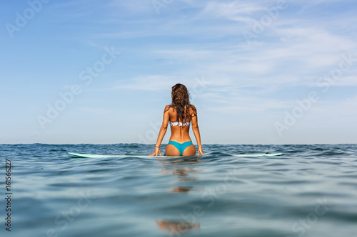 Beautiful sporty surfing girl in sexy bikini swimwear sit on big longboard surf surfboard board on sunrise or sunset and feel unity with the sea. Modern active sport lifestyle and summer vacation.