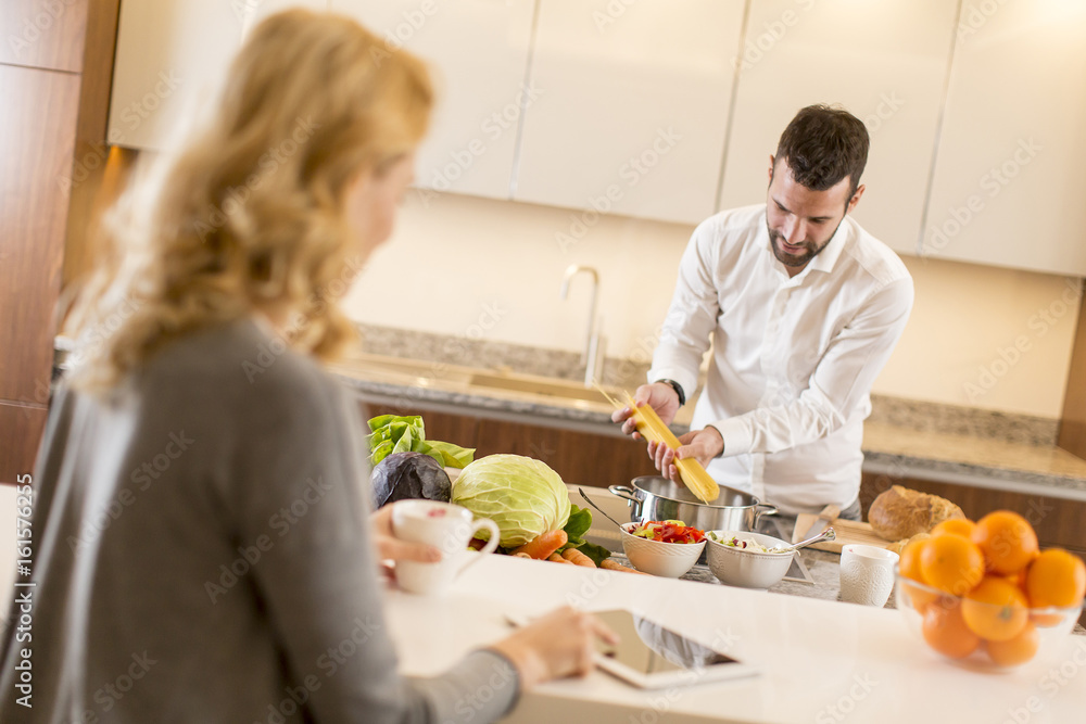 Man preparing a meal while a young woman sitting and use of tablets in a modern kitchen Man preparing a meal while a young woman sitting and use of tablets in a modern kitchen