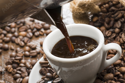 Tableau sur toile pouring coffee from coffeepot into white coffee cup, closeup.