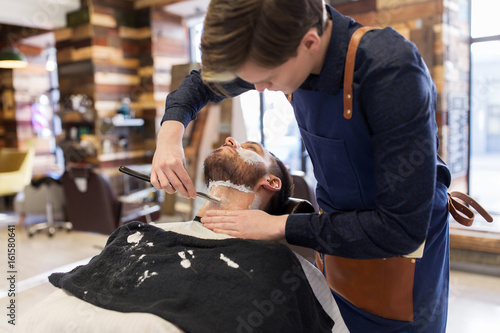 Obraz na plátně barber with straight razor shaving clients beard