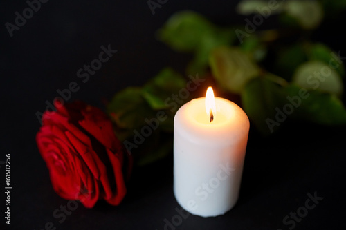 red rose and burning candle over black background