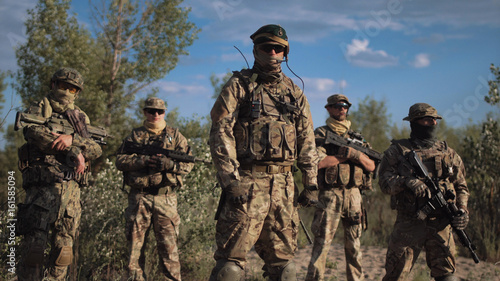 Group of soldiers in a camouflage and the hidden persons with weapon pose and look in the camera