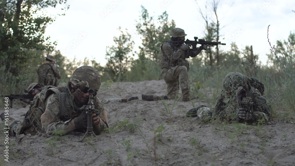 Group of military people sitting and lying with guns prepared for fight. The Commander gives the command to begin a military operation. Group of military people sitting and lying with guns prepared for fight. The Commander gives the command to begin a military operation.
