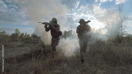Silhouettes of soldiers walking on battlefield and aiming with guns.
