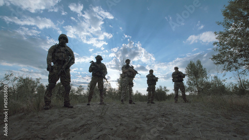 Silhouettes of cool soldiers standing in nature in a row.