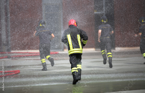 Fotografie Firefighters run under the splashes of water during fire extingu