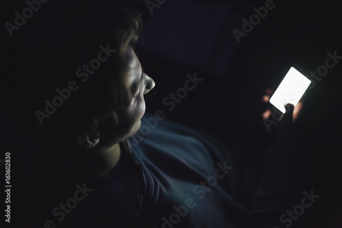 Happy teenage boy using smart phone in the dark