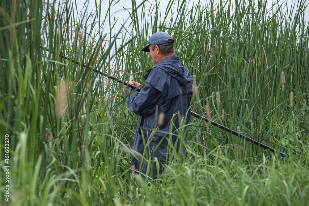 A fisherman stands on the shore of a lake pond in a forest with a fishing rod and catches fish in a jacket A fisherman stands on the shore of a lake pond in a forest with a fishing rod and catches fish in a jacket