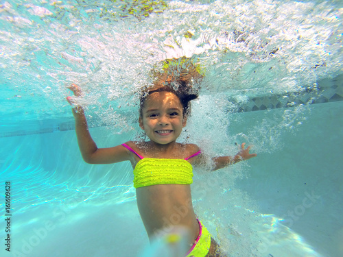 little girl swiming underwater in a pool posing to camera  photo