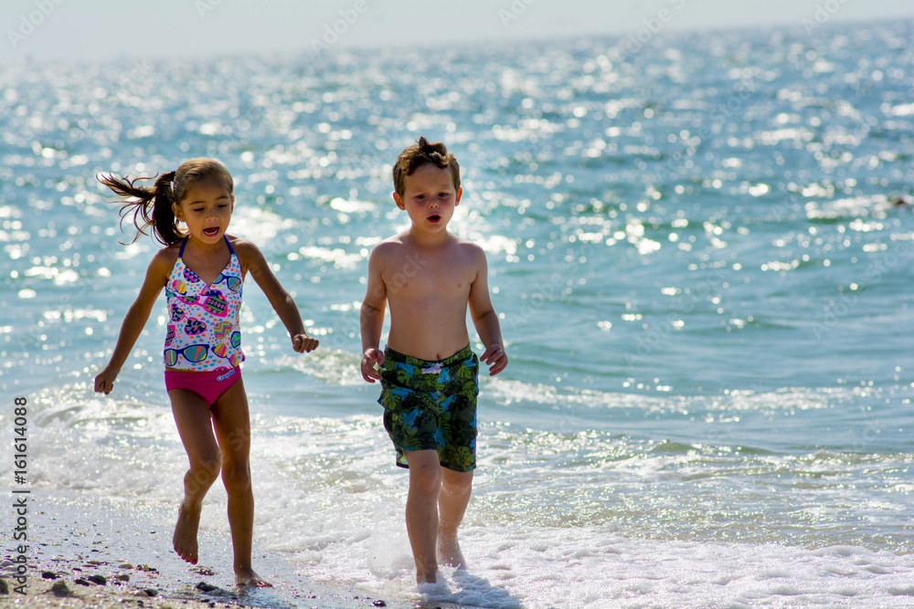 Φωτογραφία young girl and bot at the beach by the water playing togather in swim suits