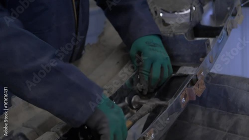  A mechanic hammers in a rivet on a car bumper