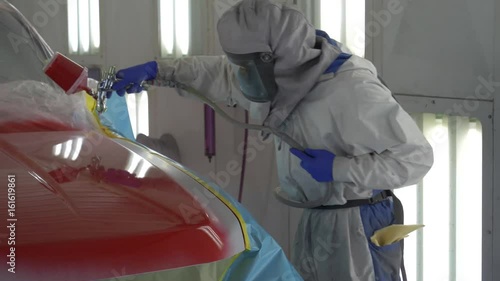 Auto bodyshop painter paints and varnishes a truck with red lacquer