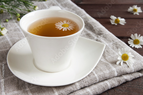 White cup with infusion of tea from daisies on a dark wooden table concept of a healthy herbal vegetable drink