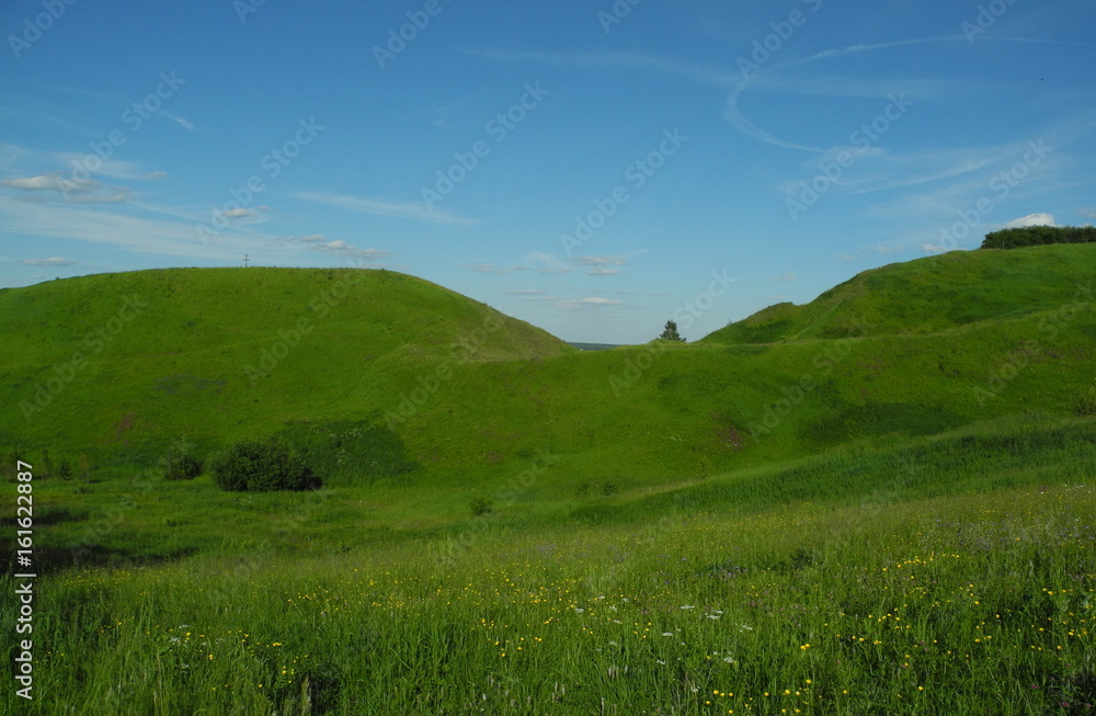 Fototapeta premium hollow between the hills covered with green grass in Sunny day