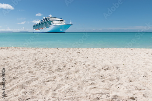 Summer tropical cruise vacation concept.
White Caribbean sandy beach with luxury cruise ship in the background