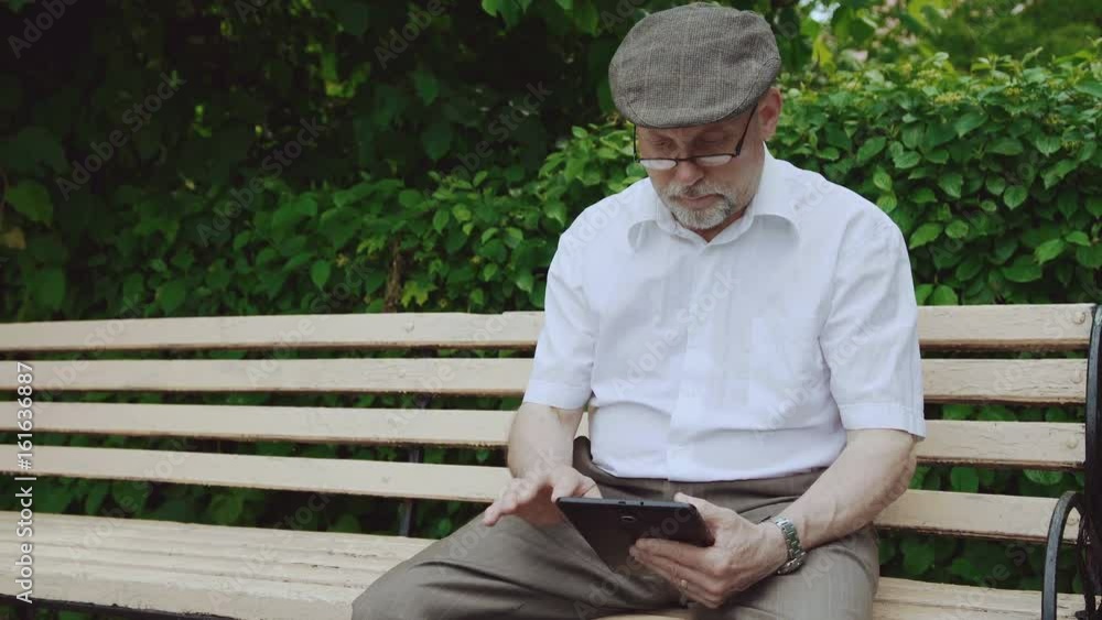 Glamorous senior man using tablet, sitting on the bench in the park 4K Glamorous senior man using tablet, sitting on the bench in the park 4K