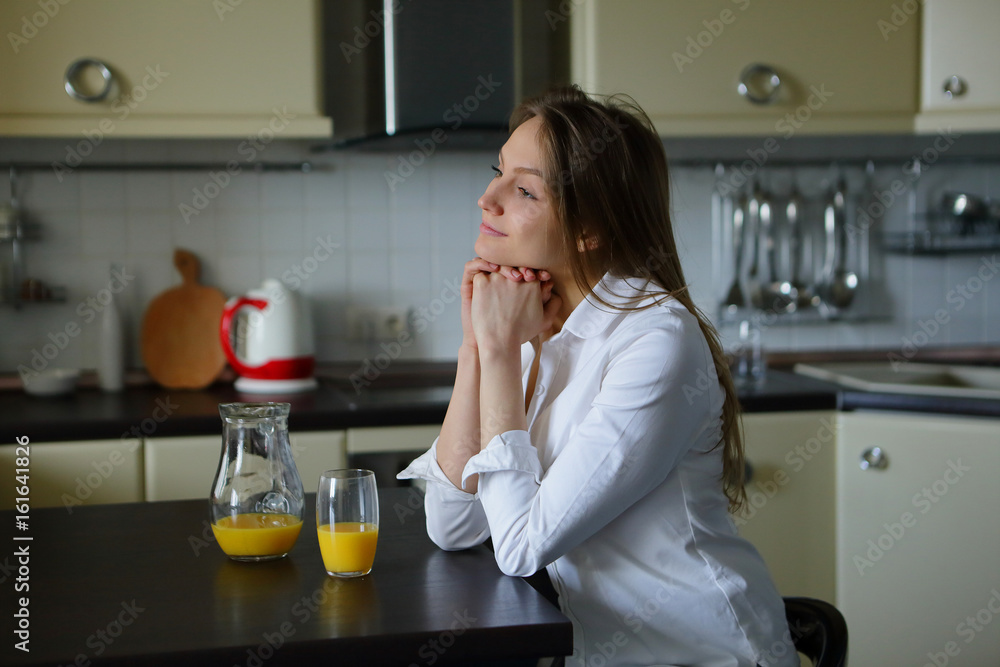Woman sitting on table, looking out the window, a healthy morning,drink, orange juice Woman sitting on table, looking out the window, a healthy morning,drink, orange juice