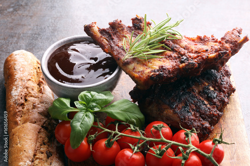 Spicy hot grilled spare ribs from a summer BBQ served with fresh tomatoes on an old vintage wooden cutting board