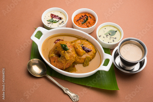 south indian food called vada sambar or sambar vada or wada dipped in sambar with coconut, green and red chutney and south indian style hot coffee, selective focus photo