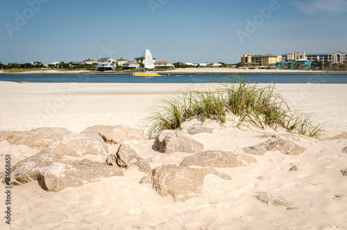 White sandy beach with rocks and foliage. Ocean bay waters with distant view of Orange beach, AL. Scenic tourist destination location.