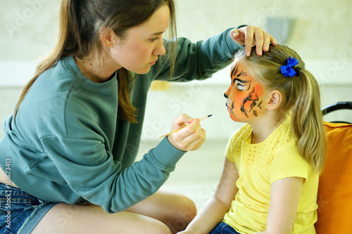 Adorable little girl getting her face painted like tiger by artist