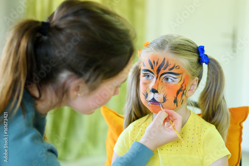 Adorable little girl getting her face painted like tiger by artist