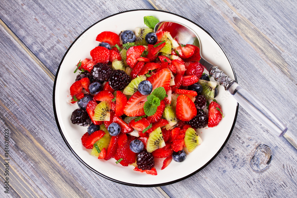 Strawberry, blackberry, blueberry and kiwi salad, garnished with mint. Fruit and berry salad. View from above, top studio shot Strawberry, blackberry, blueberry and kiwi salad, garnished with mint. Fruit and berry salad. View from above, top studio shot